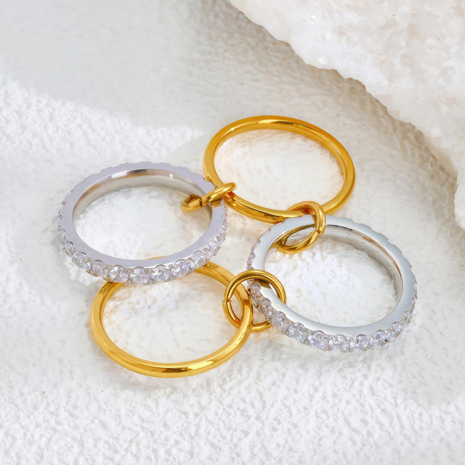 Three gold and silver rings with clear stones on a textured white surface