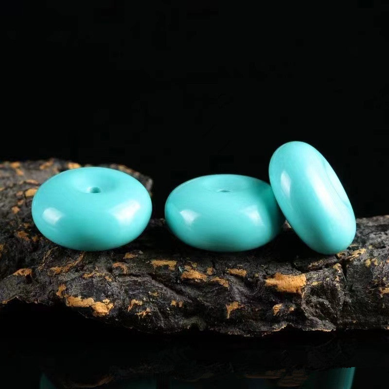 Three turquoise beads on a dark wooden surface