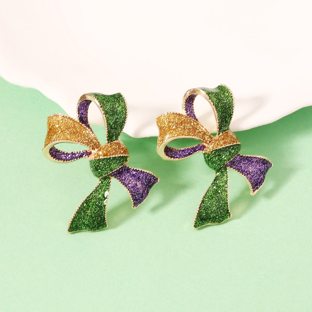 Pair of earrings shaped like green and gold ribbons with purple accents on a light green background