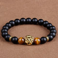 Black beaded bracelet with gold and brown accents on a brown fabric background