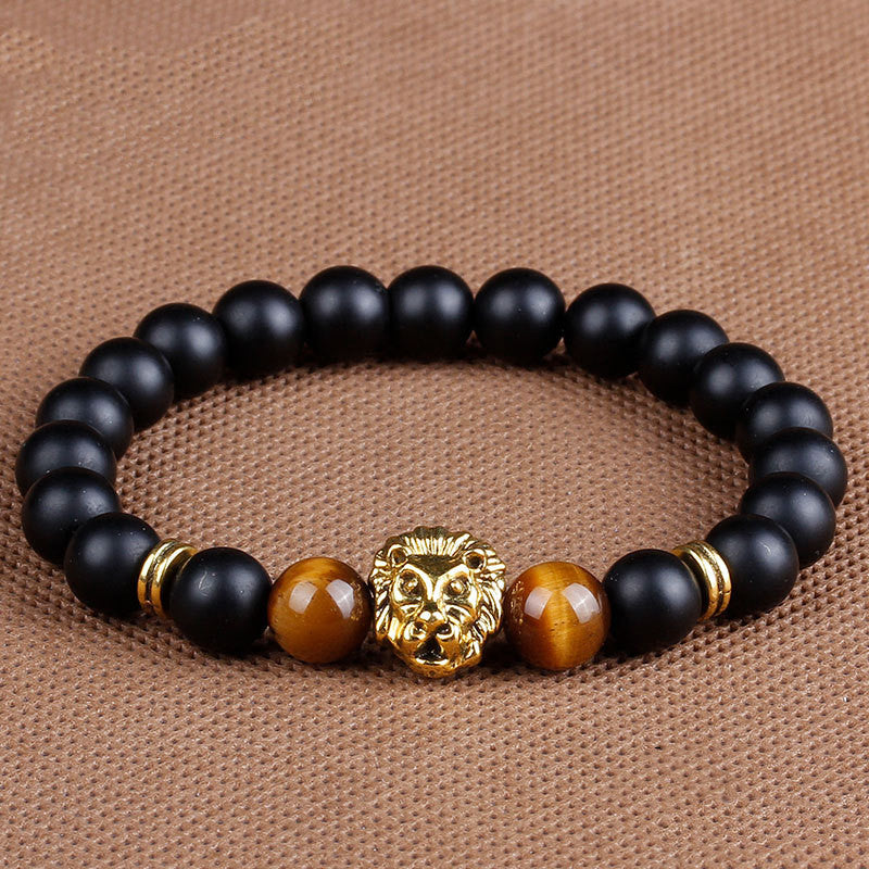 Black beaded bracelet with gold and brown accents on a brown fabric background
