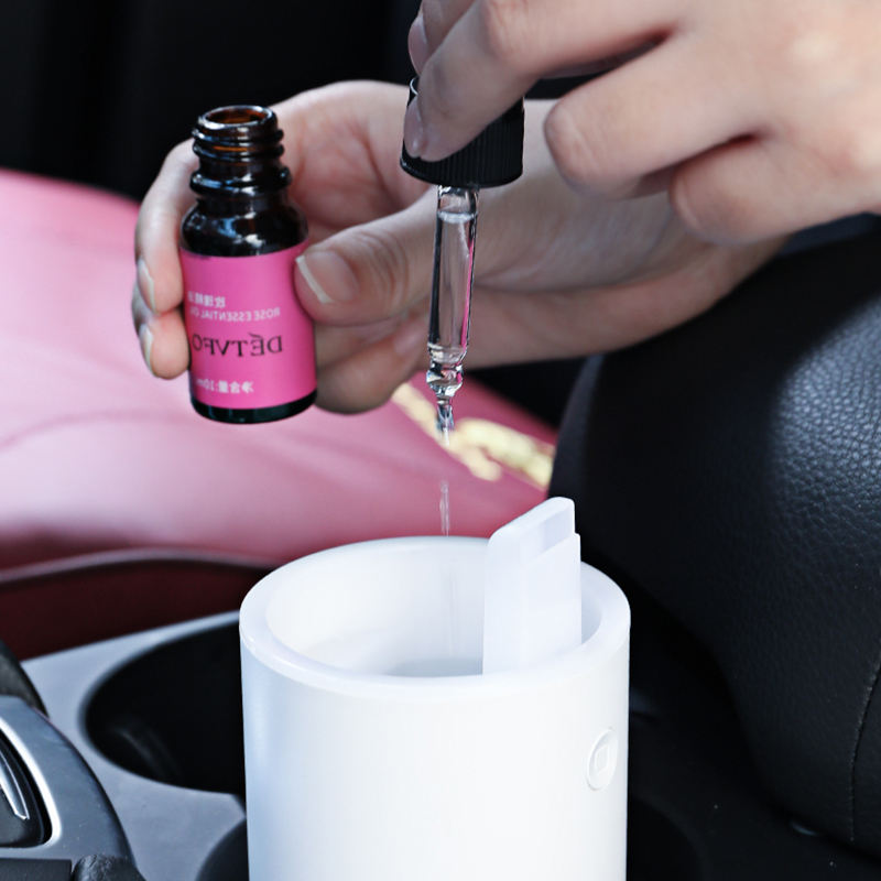 Person using a dropper to add liquid from a pink bottle into a white container inside a vehicle.