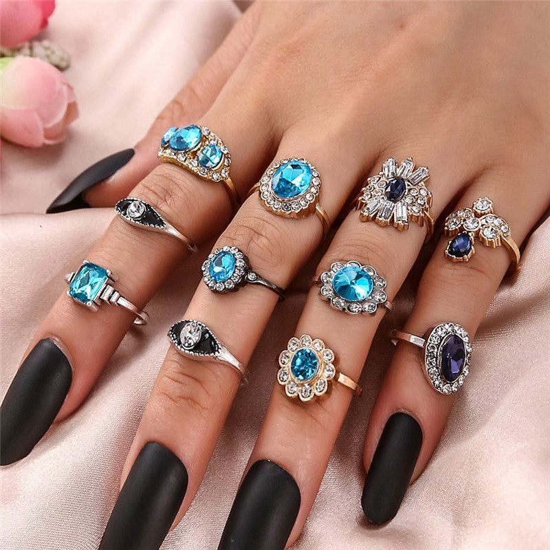 Multiple rings with blue gemstones on a hand with black nail polish.