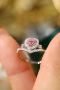 Heart-shaped pink gemstone ring with diamond accents on a finger against a blurred background