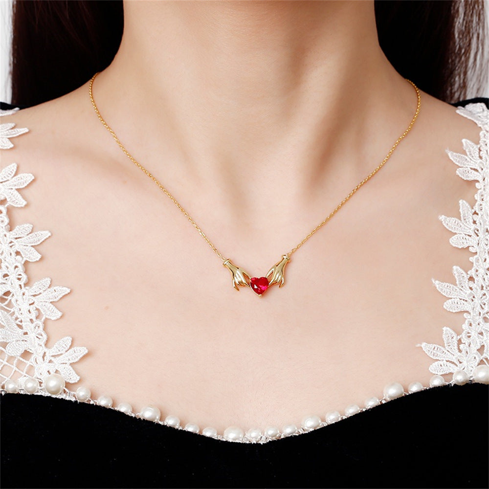 Gold necklace with a red gemstone on a person wearing a black and white lace top.